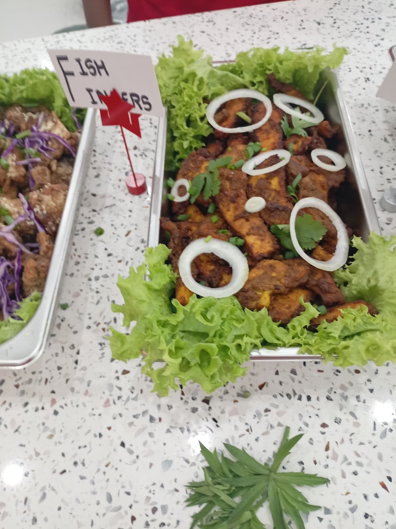 Fried fish fingers topped with onion rings and cilantro on a bed of lettuce.