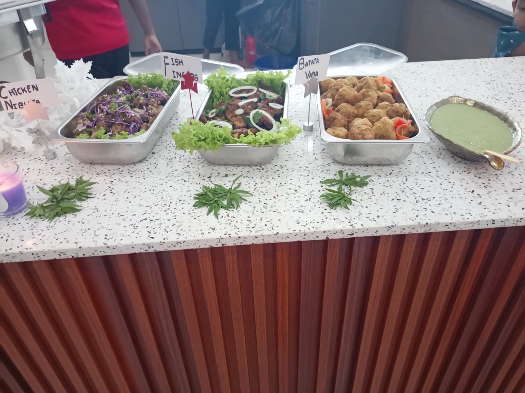 Buffet trays of chicken nibbles, fish fingers, and batata vada served with green chutney.